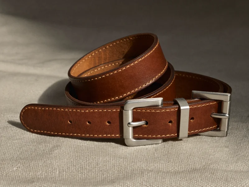 Aufgerollte braune Lederleine mit Halsband und gebürsteter Metallschnalle auf Leinenstoff